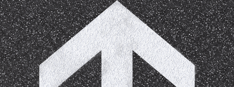 An overhead shot of a road with a large white arrow pointing upward painted on.