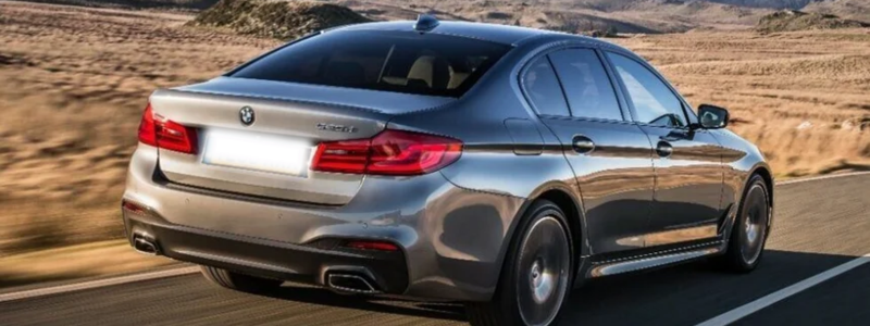 A BMW 3 Series driving in a rural desert location with sun shining down.