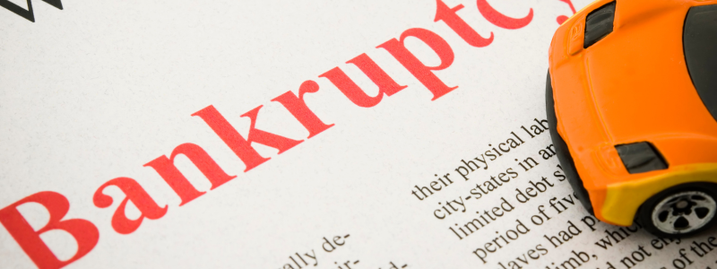 A close up of a document reading bankruptcy with a small orange car on the side of the document.