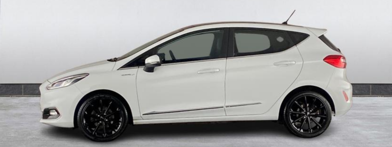 A side-on view of a cream coloured Ford Fiesta Vignale, parked against a white backdrop, likely in a car showroom.