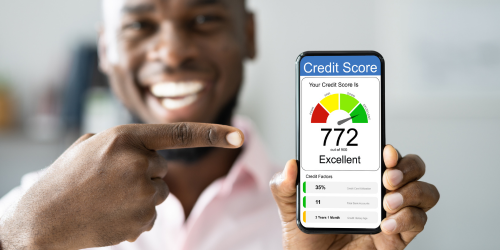 A close up of a person smiling and holding up their phone with a credit score metre on. They are pointing at the phone with the other hand.