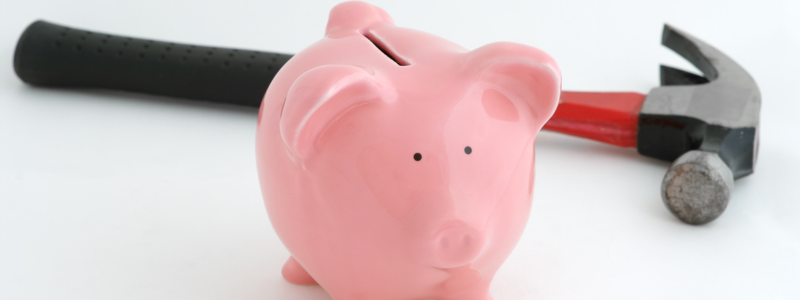 A piggy bank with a hammer laid down behind it, representing the phrase 'break the bank'.