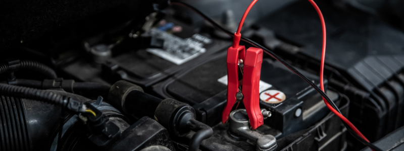 A car battery with a red jump lead attached to the positive terminal.