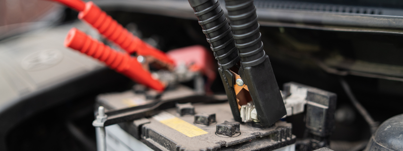 A car battery with red and black jump leads attached to different parts of the battery.