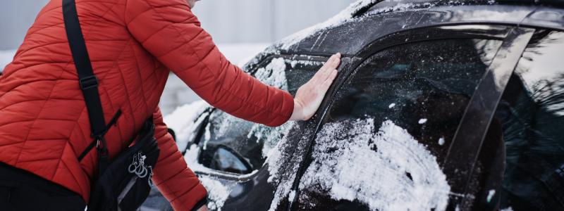 A person clearing snow off their car with their hands.