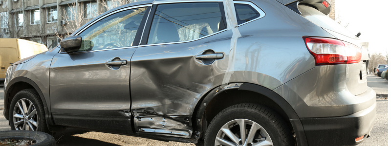 Side view of a grey SUV with significant damage to the rear door, showing the aftermath of a collision or accident.