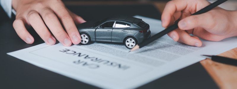 A person pointing to part of a car insurance document with someone else placing a small car on it, representing a car insurance deal.