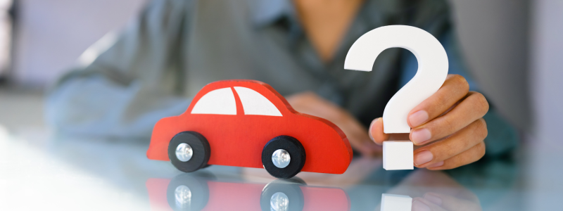 Person holding a white question mark next to a red toy car, symbolising inquiries or uncertainties related to car ownership, buying, or financing.