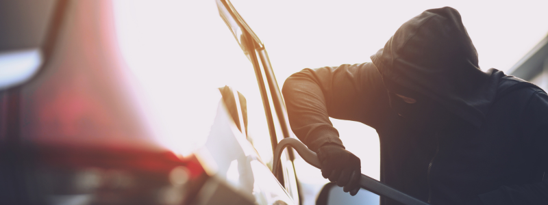 A hooded person breaks into a car with a crowbar.