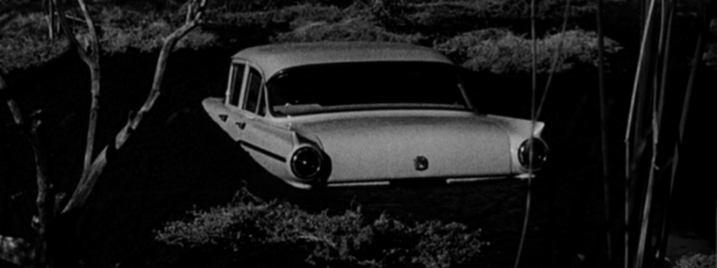 A classic white car parked into greenery and bushes, taken from the film Psycho.