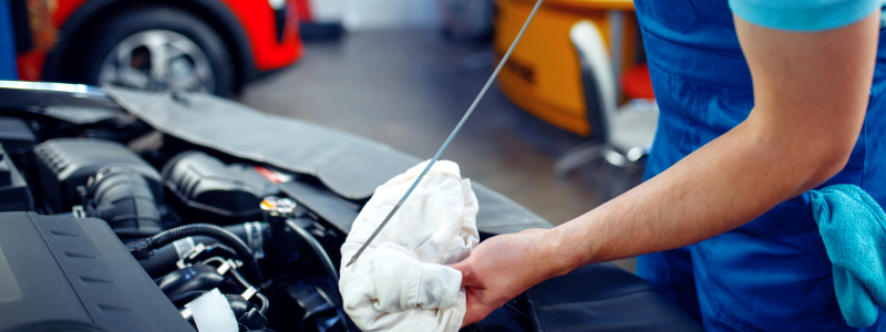 Mechanic checking car oil level with a dipstick in an automotive repair shop.