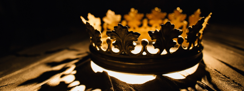 Golden crown illuminated dramatically from below, casting shadows and symbolising royalty, power, and leadership.