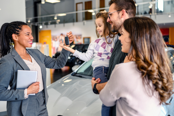 A car dealer hands over keys to a family in a dealership, symbolising a new car purchase and family cars.