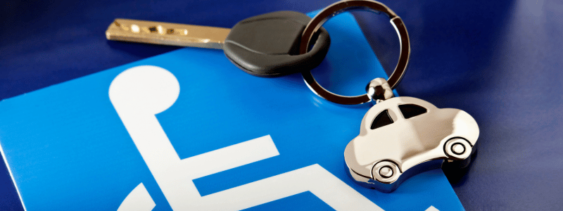 A blue disability badge with a car key and car keyring on top of it, representing disability driving.