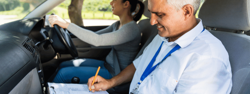 Driving instructor taking notes while a student drives during a driving test, symbolising learning, evaluation, and driver education.