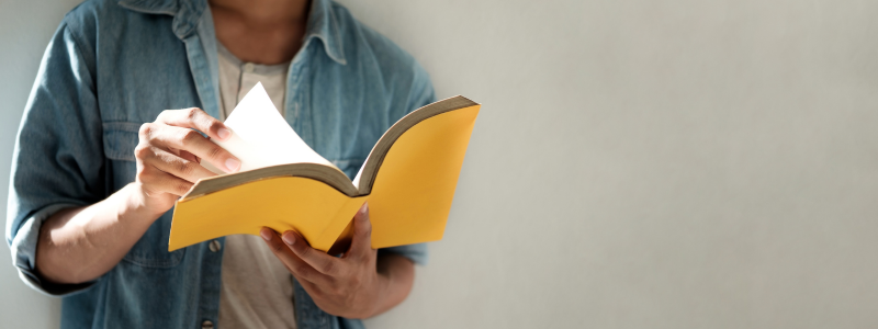 Person reading a yellow book while standing, symbolising learning, education, and personal growth.