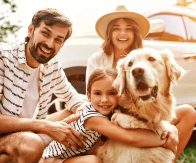 A happy family pose outside their car with a dog.