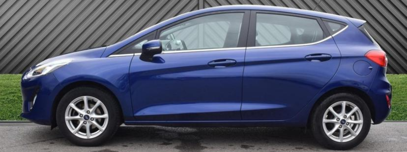 A blue Ford Fiesta Zetec parked side-on against a grey panelled wall backdrop.