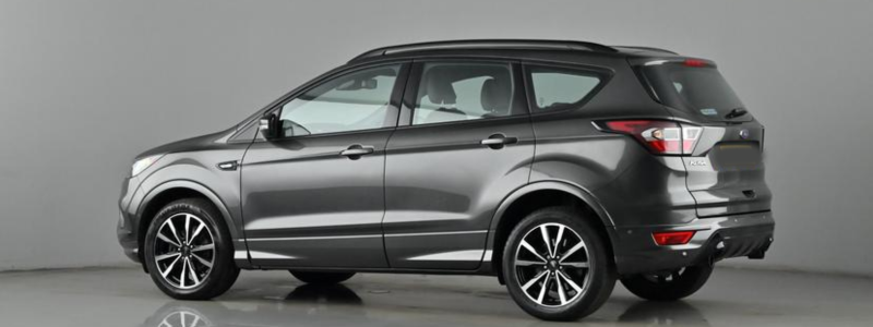 A dark grey Ford Kuga parked against a grey background, likely in a car showroom.