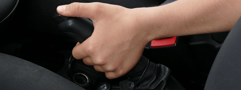 A hand pulling a handbrake up in a car.