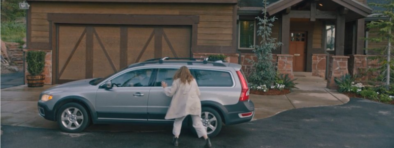 A woman stood outside an estate car in front of a house, taken from the film Hereditary.