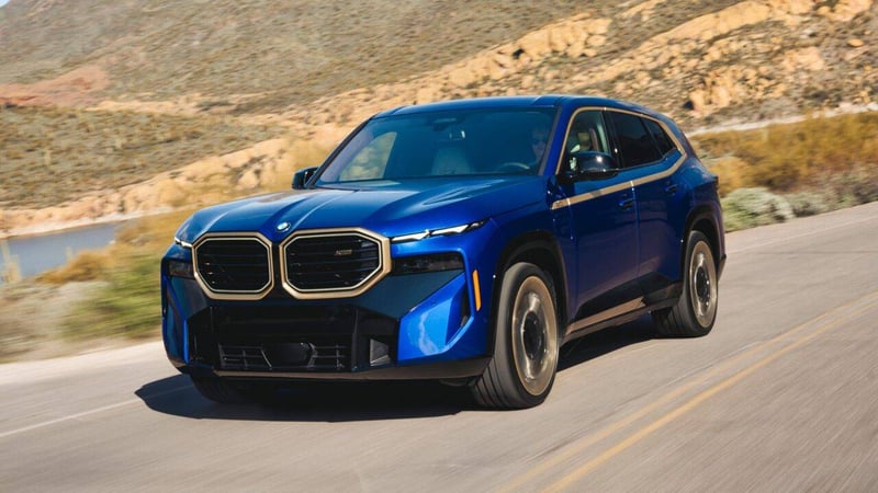 A blue BMW XM driving on a road in a rural desert location.