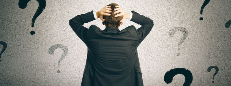 A man faced with uncertainty looking at question marks on the wall