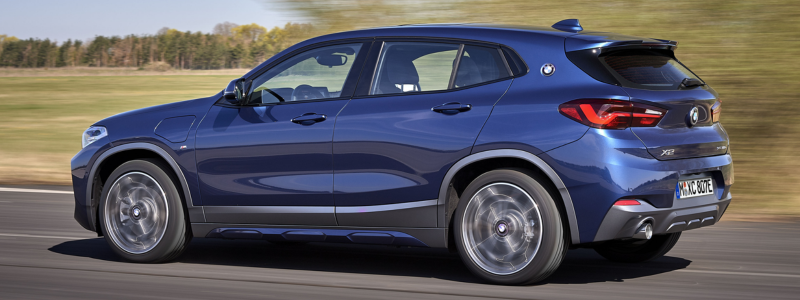 A blue BMW X2 driving on a road against a rural background.