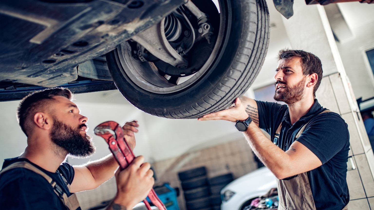 Two mechanics undertaking a car service under a car.