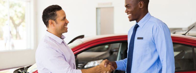 Two people shake hands in a car dealership.