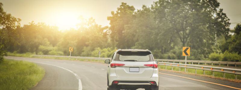 A car driving round a bend on a road, with sun shining down.