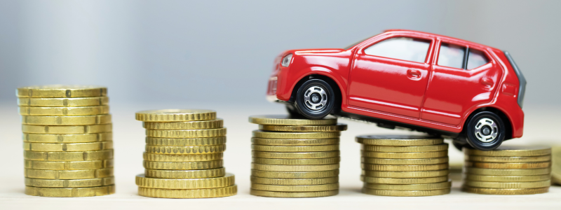 A small toy car stacked on coins rising in size from right to left.