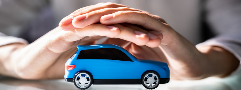 A person with two hands over a toy car, symbolising protection.