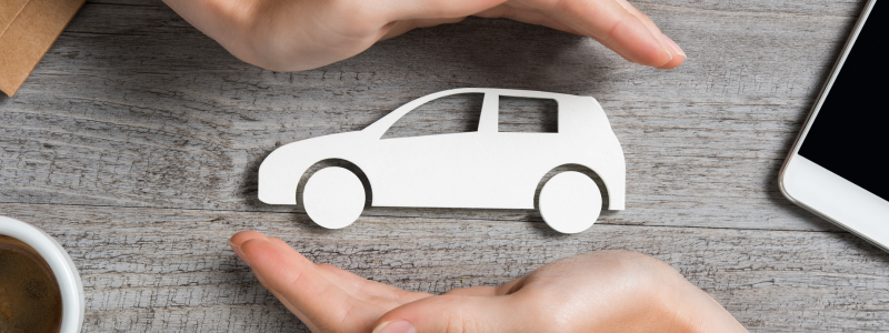 Two hands protecting a piece of paper in the shape of a car, representing car insurance and protection.