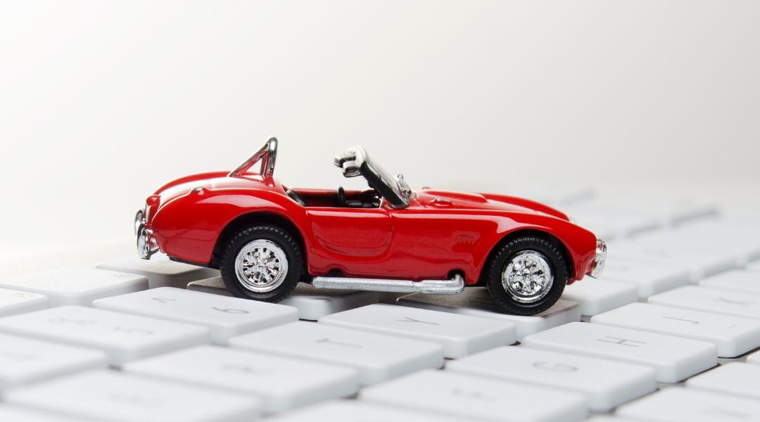 A red toy car on top of a keyboard. 