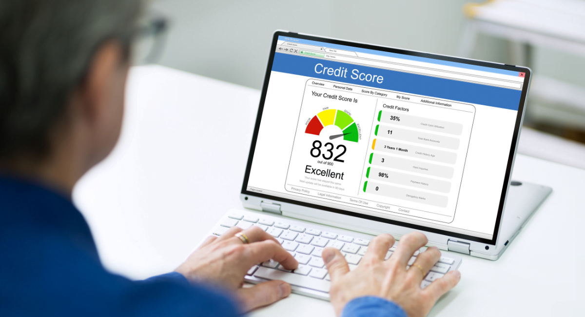 A man in a blue shirt looks towards his desktop which has a credit report on.