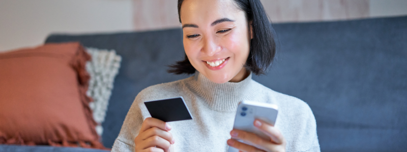 A person holds a debit card whilst using their phone.