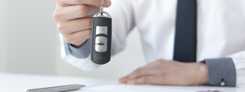 A suited person holds car keys up with their hand.