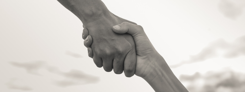 One hand reaches out to another hand and connects with it as a handshake.