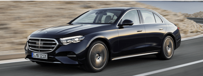 A black Mercedes Benz E-Class driving along a road with a small rockface on the side of the road.