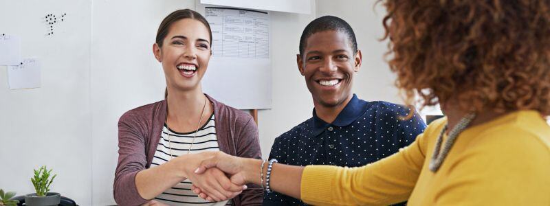 A couple shake hands with a person.