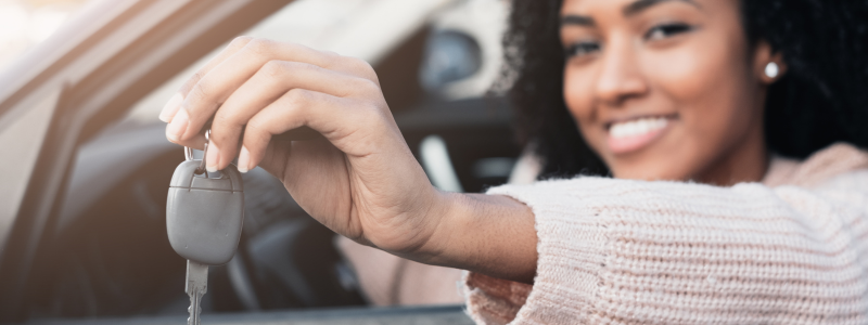 A person holds a car key out of their car window.