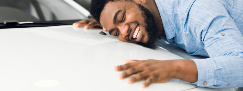 A person leans on their car bonnet smiling, symbolising a driver happy with their car.