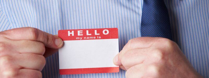 A suited person holds an empty name tag in their hands.