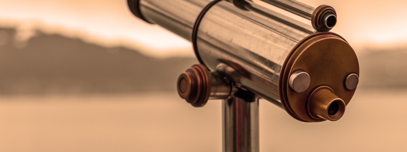 A close up of a classic telescope pointing out over water and hills.