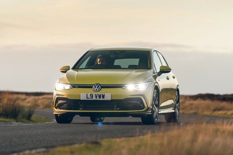 A yellow VW Golf driving on a rural road.