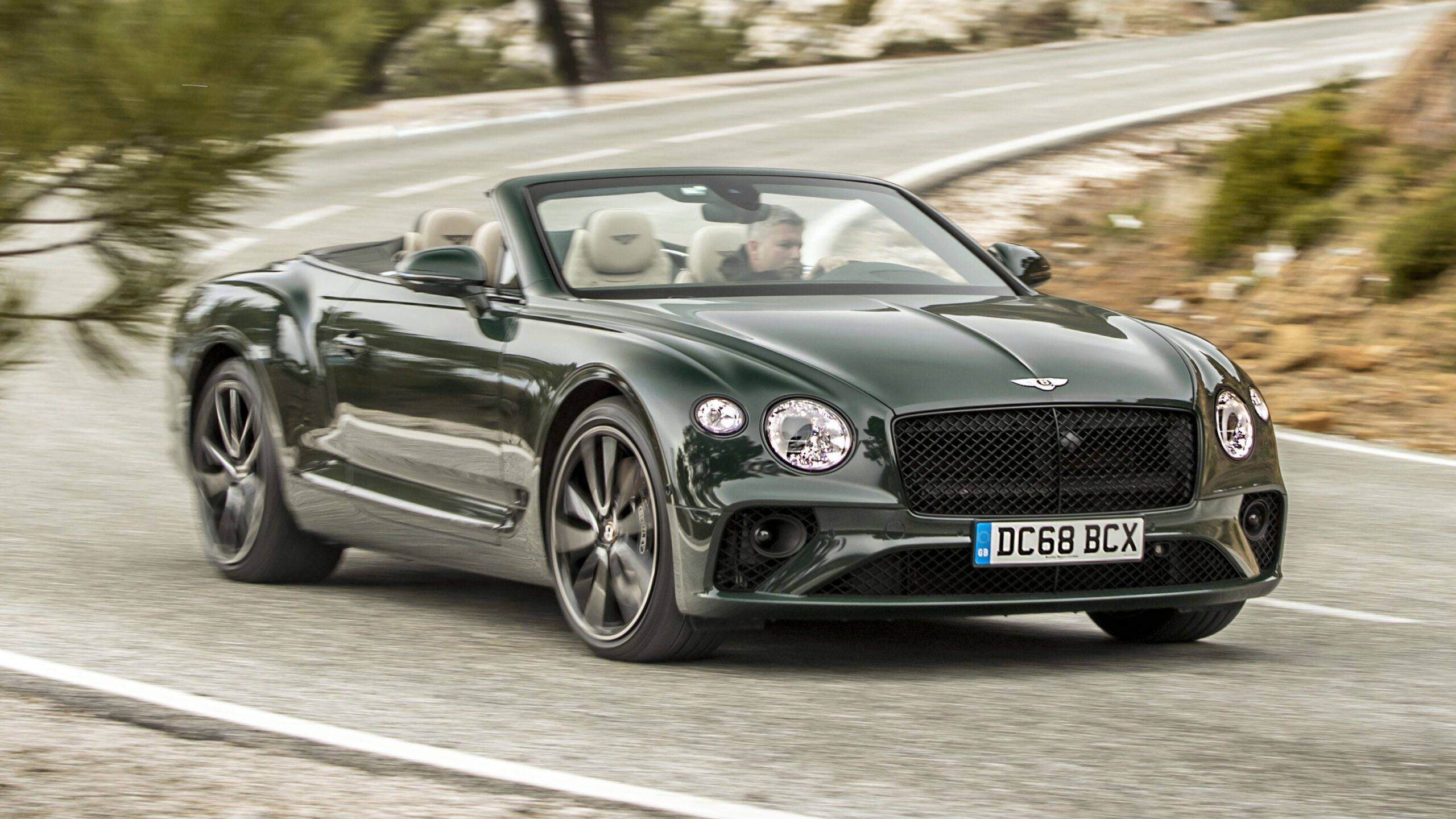 The Bentley Continental GTC in emerald green driving on a road.