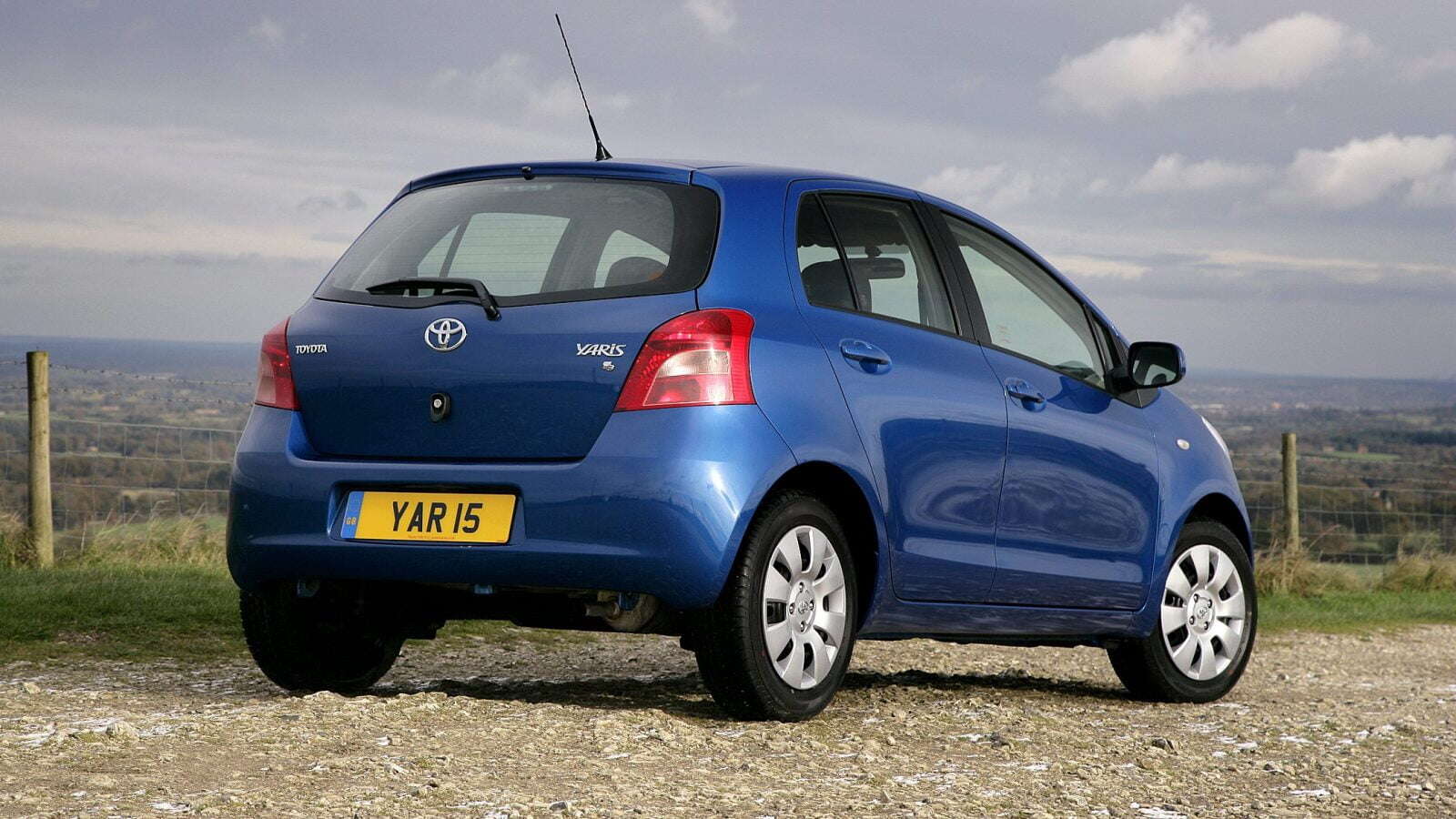 A blue Toyota Yaris parked up overlooking hills and a town.