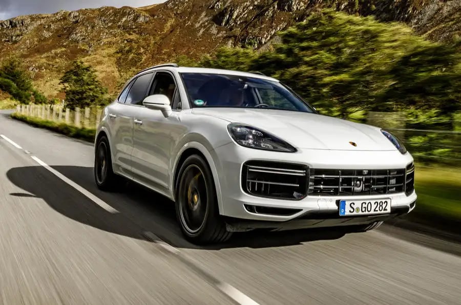 A white Porsche Cayenne on an open road with sun shining on it.