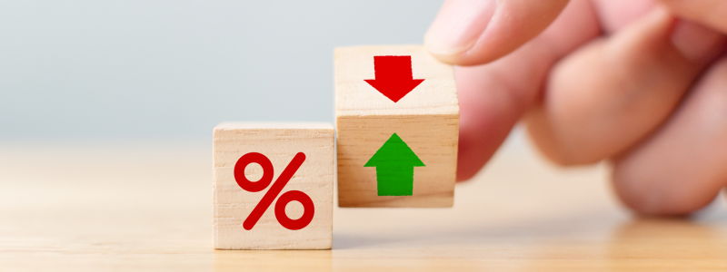 Hand adjusting wooden blocks with percentage sign and red down arrow on one side, and green up arrow on the other.